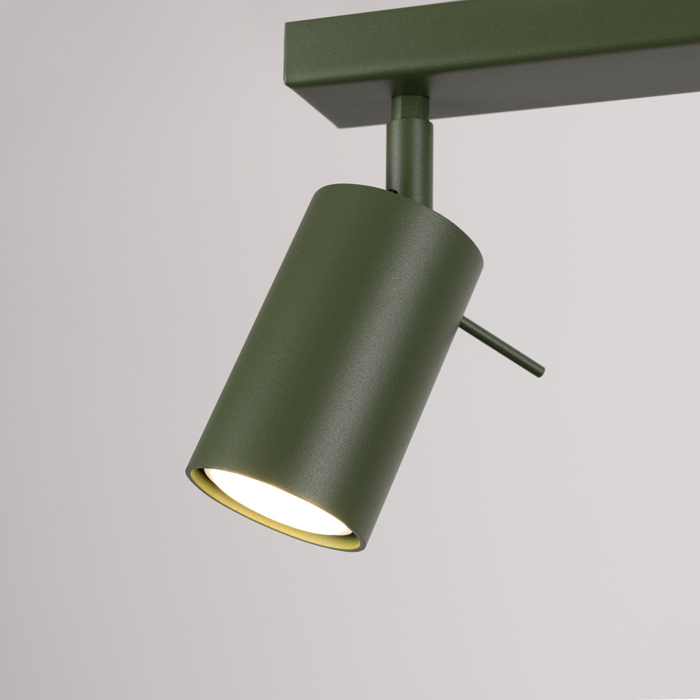 Minimalistischer olivegrüner Deckenstrahler mit zylindrischem Design und verstellbarem Lichtwinkel an rechteckiger Halterung.