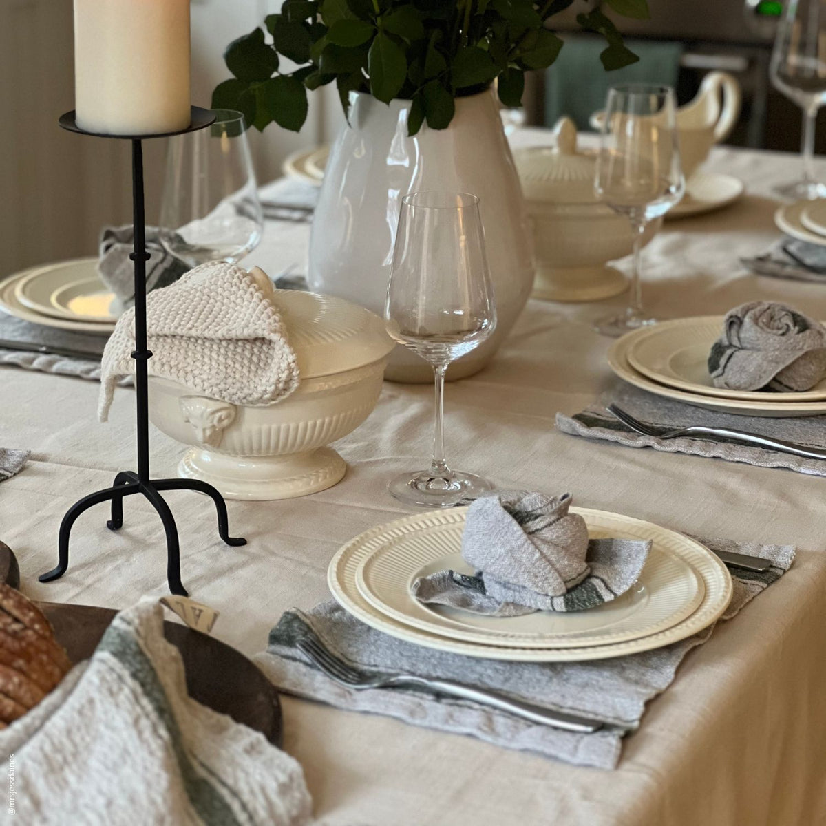 Festlich gedeckter Esstisch mit Leinentischdecke, Kerzenhalter, Keramikgeschirr und Stoffservietten im eleganten Landhausstil.