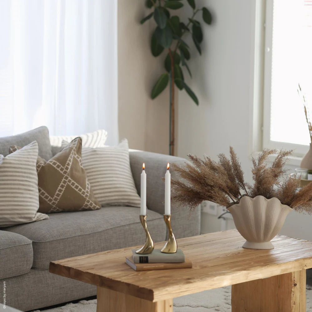 Wohnzimmer im Landhausstil mit grauem Sofa, Zierkissen, rustikalem Holztisch, Kerzenhaltern und Vase mit Trockenblumen.