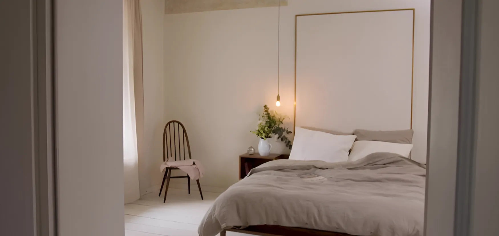 Einblick in ein minimalistisches Schlafzimmer mit Naturtönen, gemütlichem Bett, Hängelampe und frischen Blumen auf dem Nachttisch.