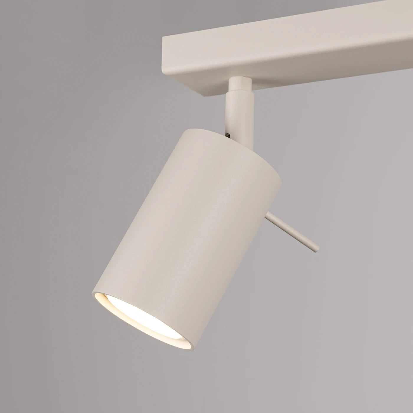 Minimalistischer weißer zylindrischer Schienenstrahler mit neigbarem Kopf an horizontaler Schiene vor hellem Hintergrund