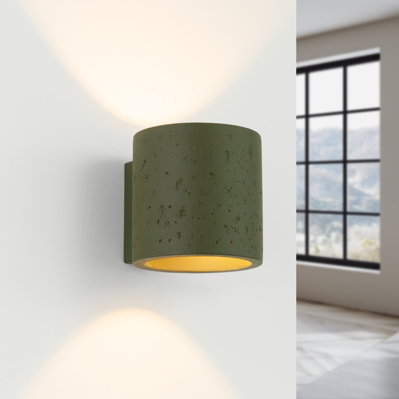 Grüne ORBIS Wandleuchte aus Beton mit warmem Up- und Downlight an heller Wand mit modernem Raumhintergrund