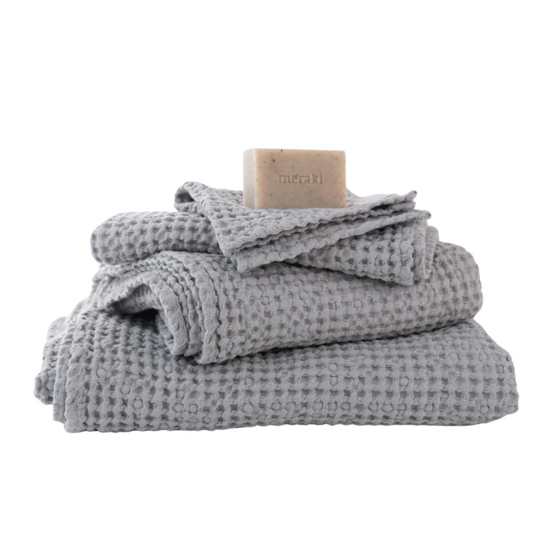 Grau gefaltete Waffelpiqué-Handtücher mit naturfarbener Seife im minimalistischen Spa-Stil arrangiert.