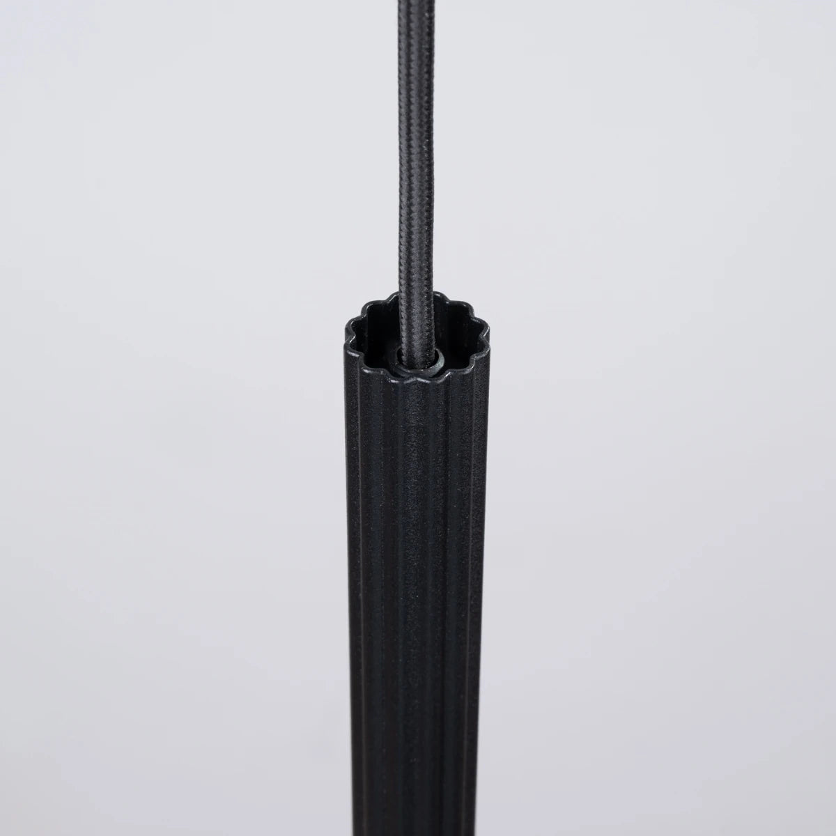 Detail der Pendelleuchte CORA 1 in Schwarz – elegant gerilltes Aluminiumgehäuse mit schwarzem Textilkabel in minimalistischem Stil.