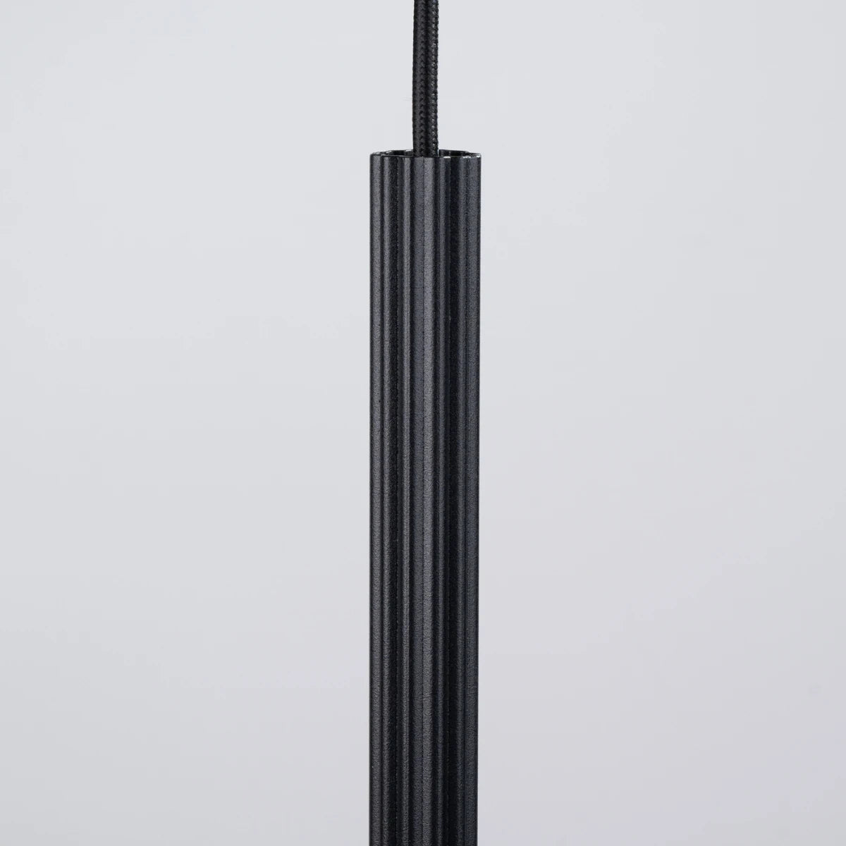 Detailansicht der Pendelleuchte CORA 1 in Schwarz – elegante Rillenstruktur aus Aluminium, kombiniert mit schwarzem Textilkabel.